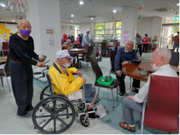 吳雲龍（左1）協助行動不便同袍推輪椅至餐桌就定位， 貼心為同袍盛湯麵，讓同袍備感溫馨