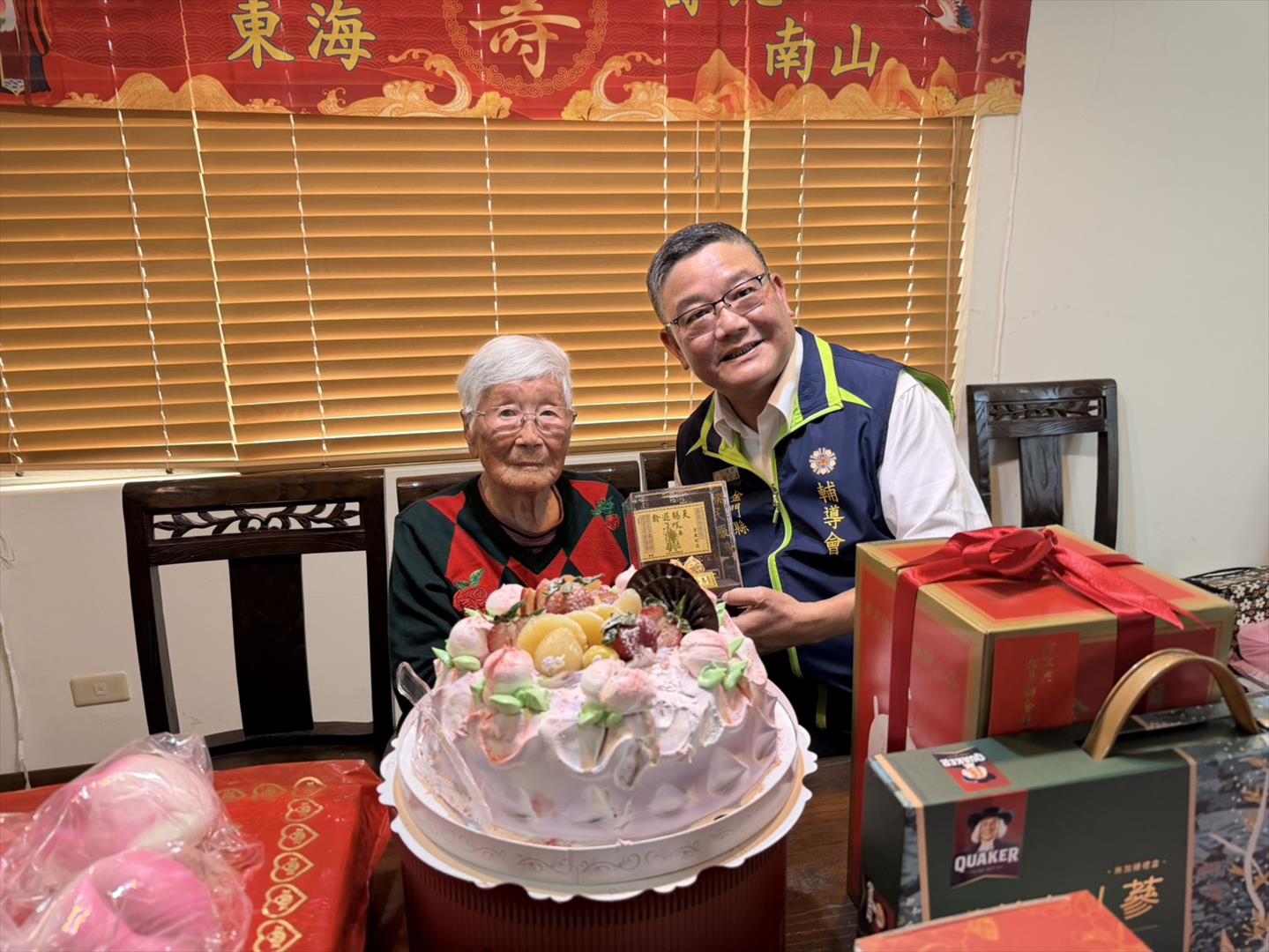 劉信義處長（右）代表主任委員嚴德發致贈壽星李許八奶（左）金壽桃。