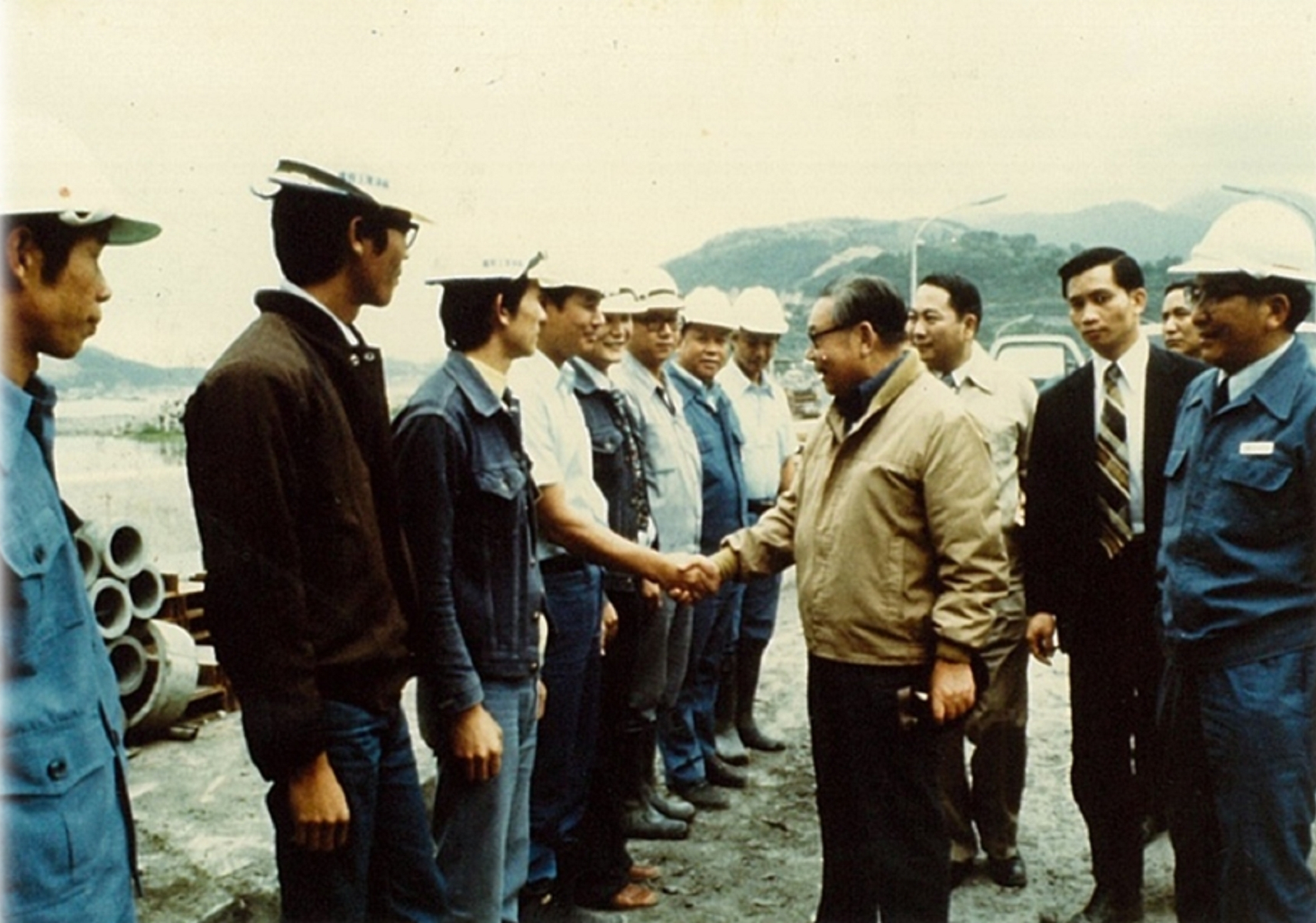 民國64年10月26日行政院長經國先生視察「十大建設」之「台中港」建港工地，與港區施工的榮民工程處員工握手致意。